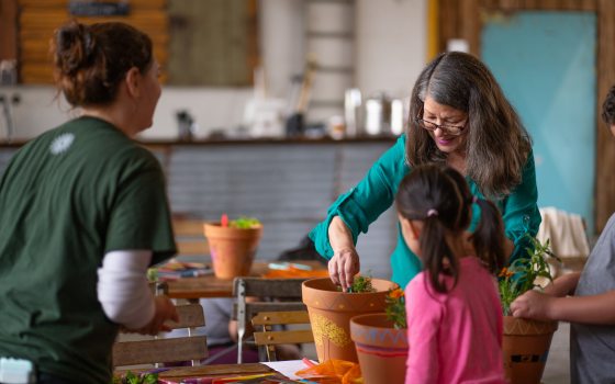 three people planting a a plant in a painted terra cotta pot